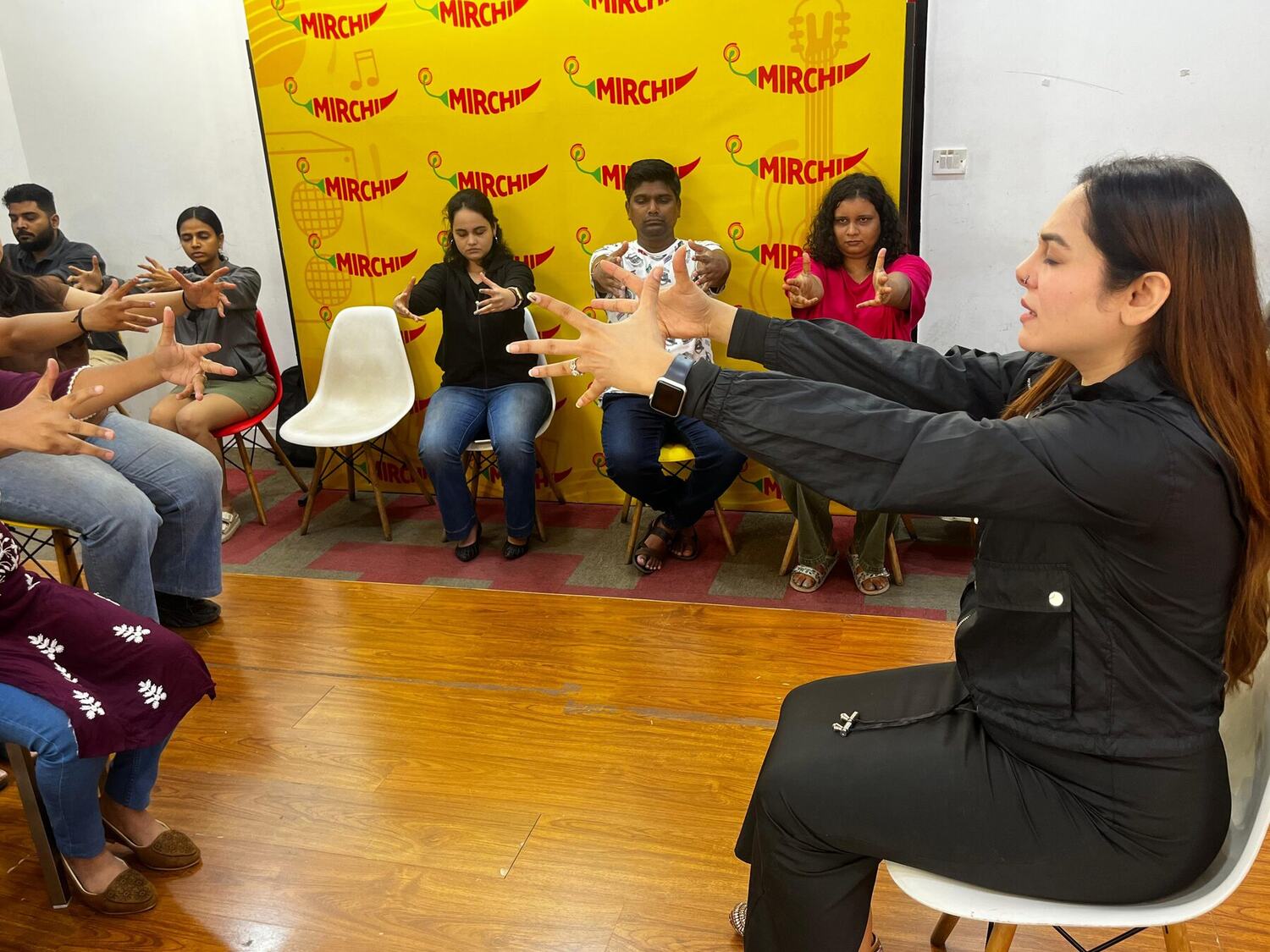 Vibha Jain seated facing a semicircle of participants, all extending their arms forward during a guided group exercise.